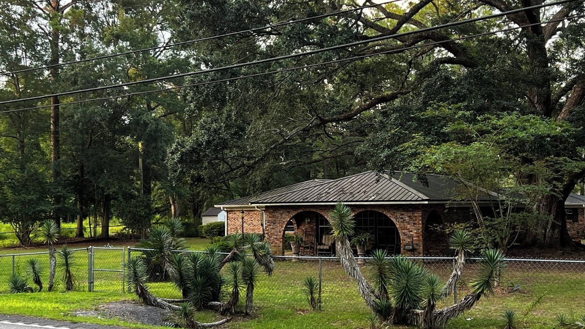 Moss Point House | Large fenced in home under a giant, moss covered, southern oak tree.